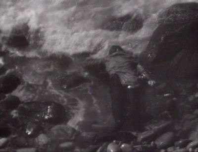 Face down in the water, wearing an overcoat, with a flask in his back pocket